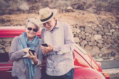 Senior couple using smart phones while standing by car