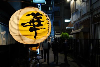 People walking on illuminated street amidst buildings at night