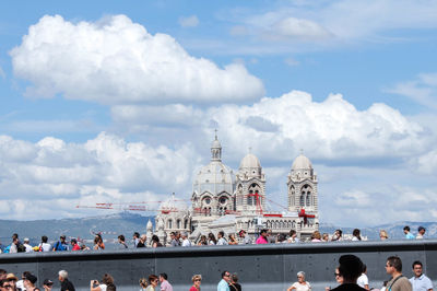 Group of people in front of building against cloudy sky