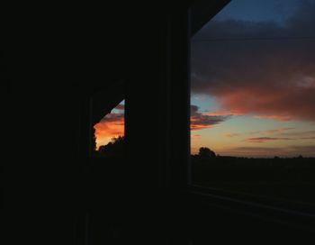 Silhouette built structure against cloudy sky seen through window