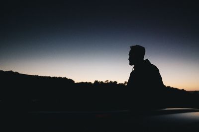 Silhouette man sitting against sky at sunset