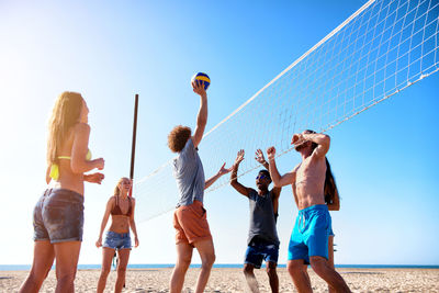 Rear view of people enjoying at beach against clear sky