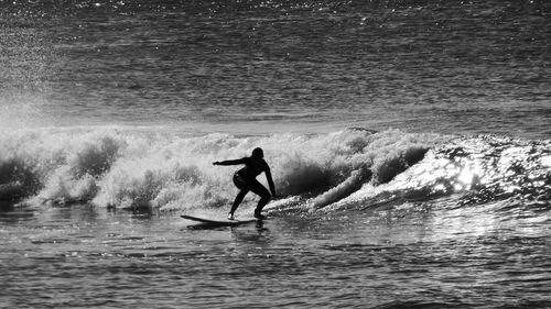 Full length of silhouette woman surfing in sea on sunny day