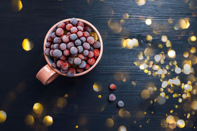 Full mug of fresh frozen cranberries on dark rustic background with christmas bokeh lights. toned