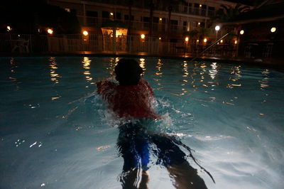 Rear view of woman swimming in pool at night