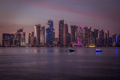 Illuminated modern buildings by sea against sky