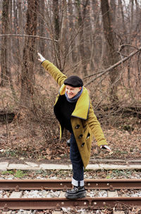 Smiling woman with arms outstretched standing on railroad track during winter