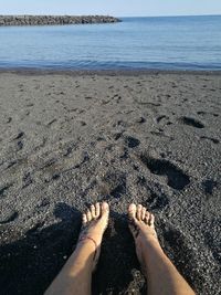 Low section of woman sitting on sand at beach