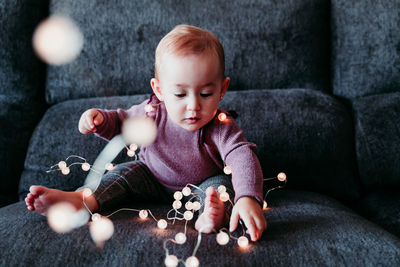 Cute smiling baby girl with decoration sitting on sofa at home