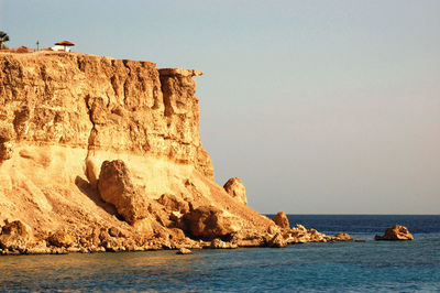Rock formations by red sea against sky