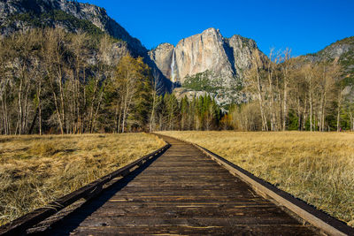 Dirt road leading towards mountains against clear sky