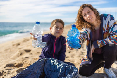 Mother and son picking plastic and garbage on the beach. focus on the bootles