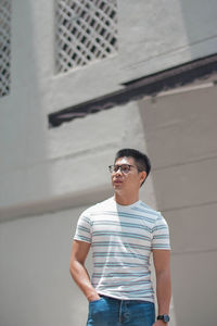 Young man wearing sunglasses standing against wall in city