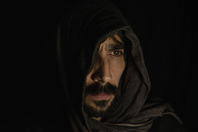 Face of a young man covering his face with a dark scarf on a black background