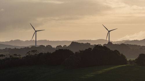 Wind turbines on field against sky during sunset