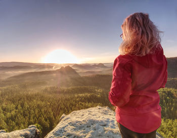 Girl watch sun rising at horizon. spring valley with stripped mist and sticking out treetops