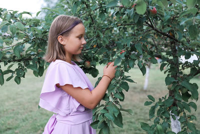 Side view of young woman standing against plants