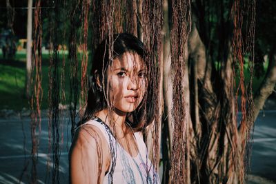 Portrait of young woman standing by tree trunk in forest