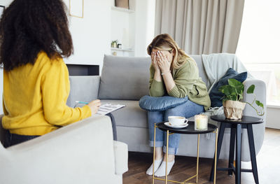 Side view of woman using mobile phone while sitting on sofa at home