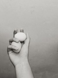 Cropped image of hand holding eggs against wall