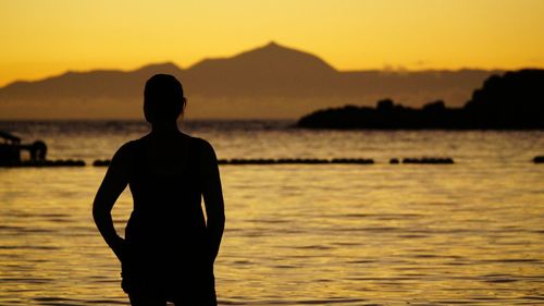 Silhouette of woman standing at beach during sunset