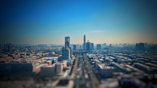 Tilt-shift image of buildings in city against clear blue sky