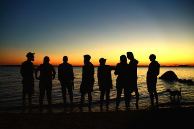 Silhouette people standing on beach against clear sky during sunset