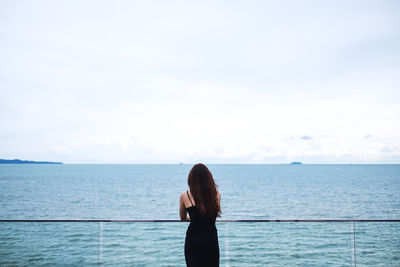 Rear view of woman standing by sea against sky