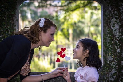 Mother giving heart shape decoration to daughter standing by built structure