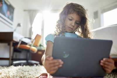 Low angle view of girl using tablet computer while kneeling on rug in bedroom
