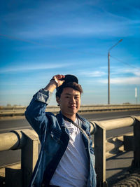 Young man looking away while standing against sky