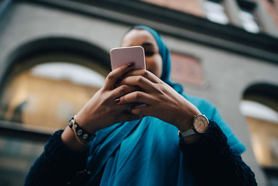 Low angle view of young woman using smart phone against building in city