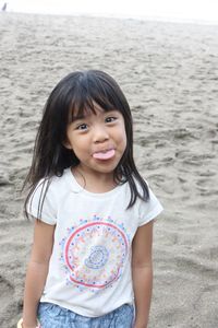 Portrait of girl sticking out tongue while standing at beach