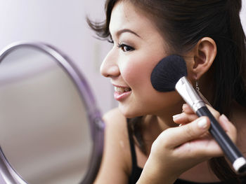 Close-up of smiling young woman applying make-up with brush