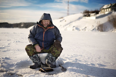 Full length of senior man ice fishing in frozen lake