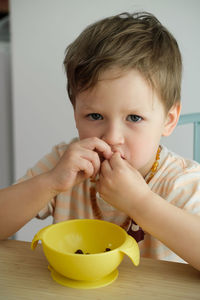 Toddler boy eating happily by the table food by himself in the room. child having meal. happy kid