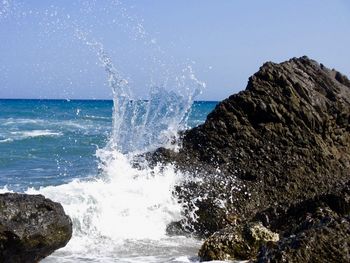 Sea waves splashing on rocks against clear sky