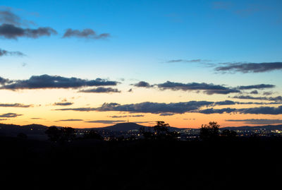 Silhouette city against dramatic sky during sunset