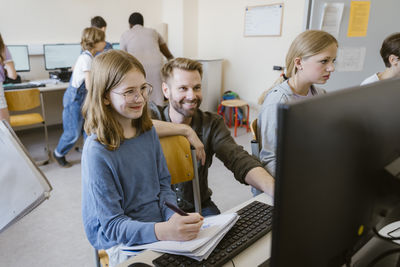 Smiling male teacher with students learning at computer class in school