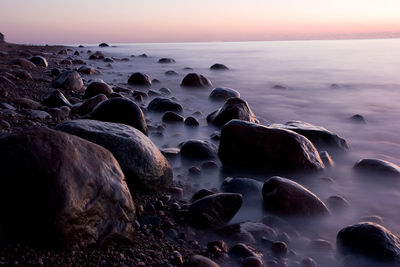 Rocks at sea shore against sky during sunset