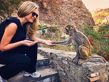 Full length of woman giving food to monkey while crouching on staircase