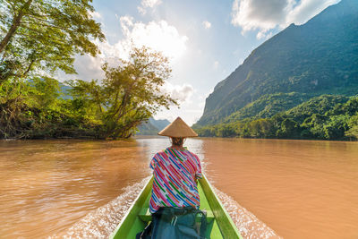Rear view of woman on boat in river against sky