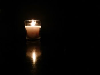 Close-up of illuminated candle on table in darkroom