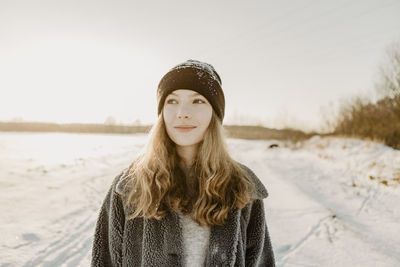 Portrait of beautiful teenage girl standing outdoors and smiling against rising winter sun