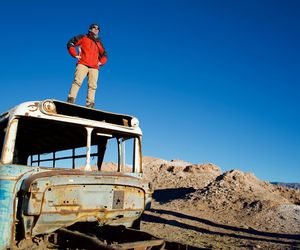 Low angle view of mid adult man standing on abandoned bus against clear blue sky during sunny day