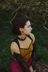 Young woman looking away while sitting on land