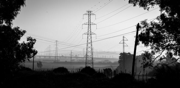 Low angle view of silhouette trees and electricity pylon against sky
