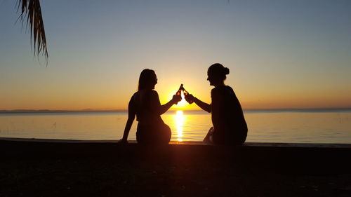 Silhouette people on beach against clear sky during sunset