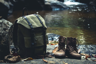 Close-up of backpack and boots on rock against river