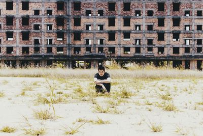 Portrait of man sitting on field against abandoned building